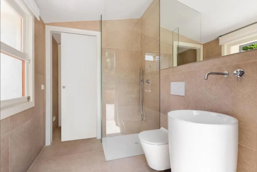 Un baño con azulejos, ducha de vidrio, inodoro y lavabo independiente.