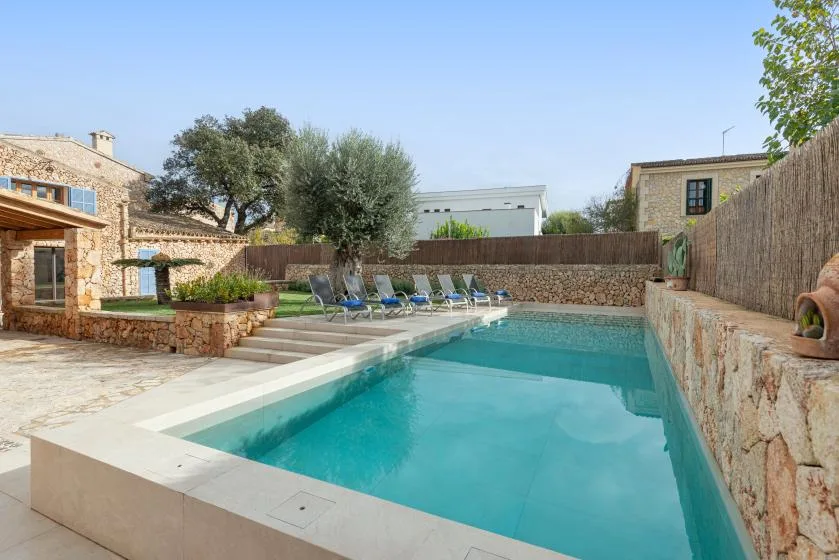 Una piscina junto a un patio de piedra, con asientos reclinables al borde.