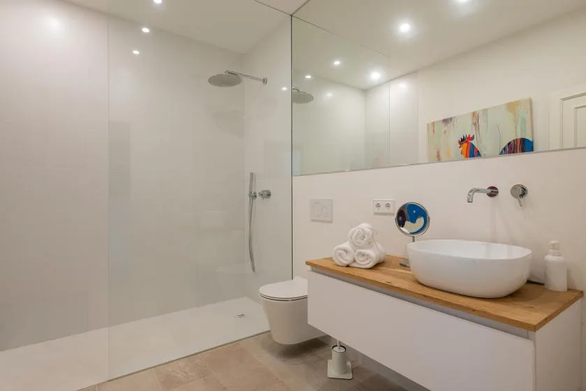 Un baño luminoso con ducha a ras de suelo y lavabo sobre una encimera de tono madera.
