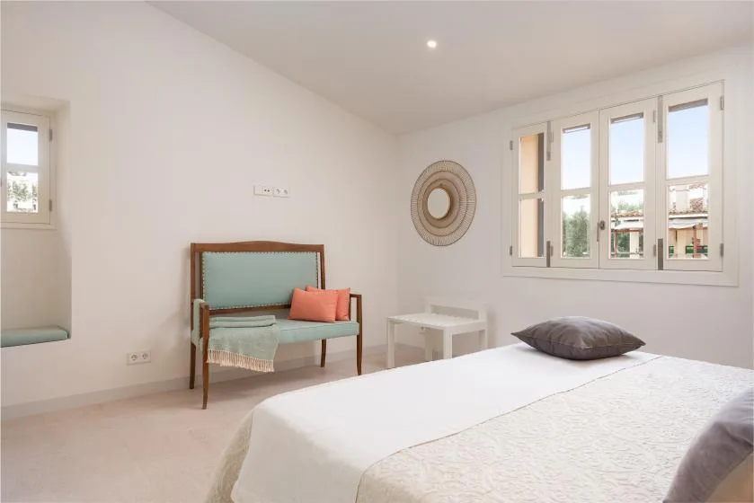 Un dormitorio luminoso con cama, asientos y grandes ventanas.