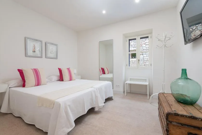 Un dormitorio luminoso con ropa de cama blanca, almohadas de rayas rosas y una ventana.