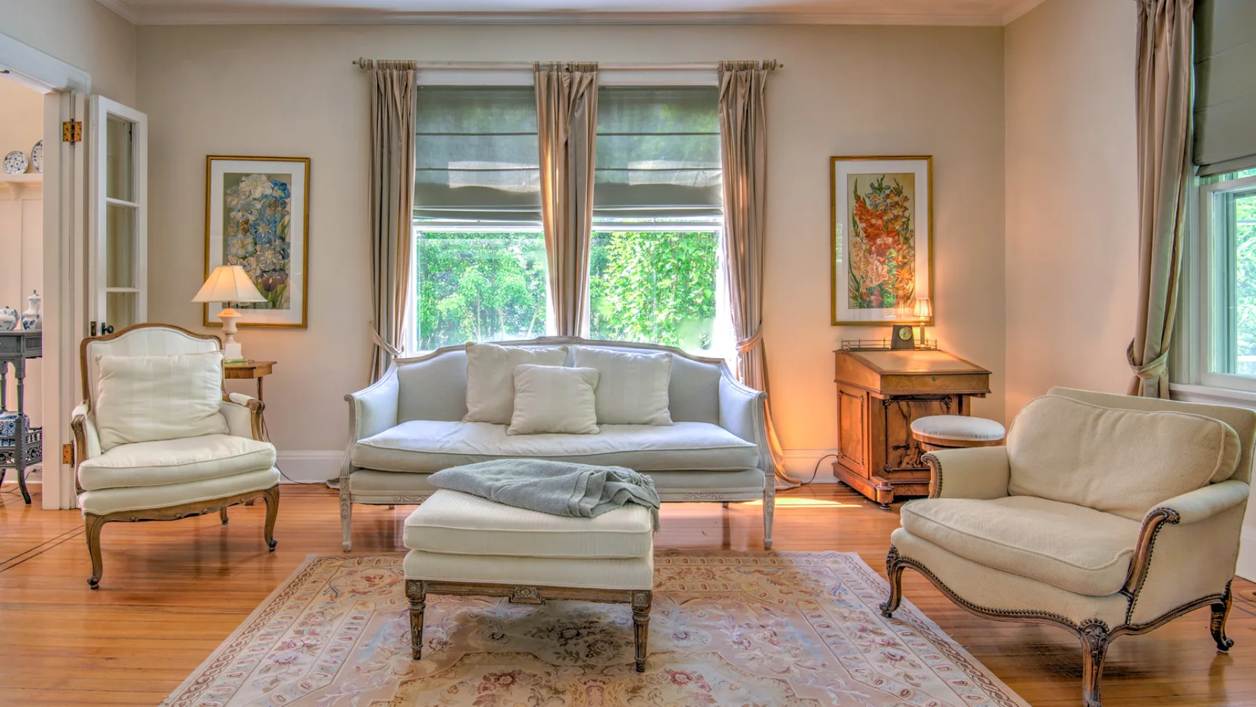 A living room with seating arranged around a central ottoman and large windows.