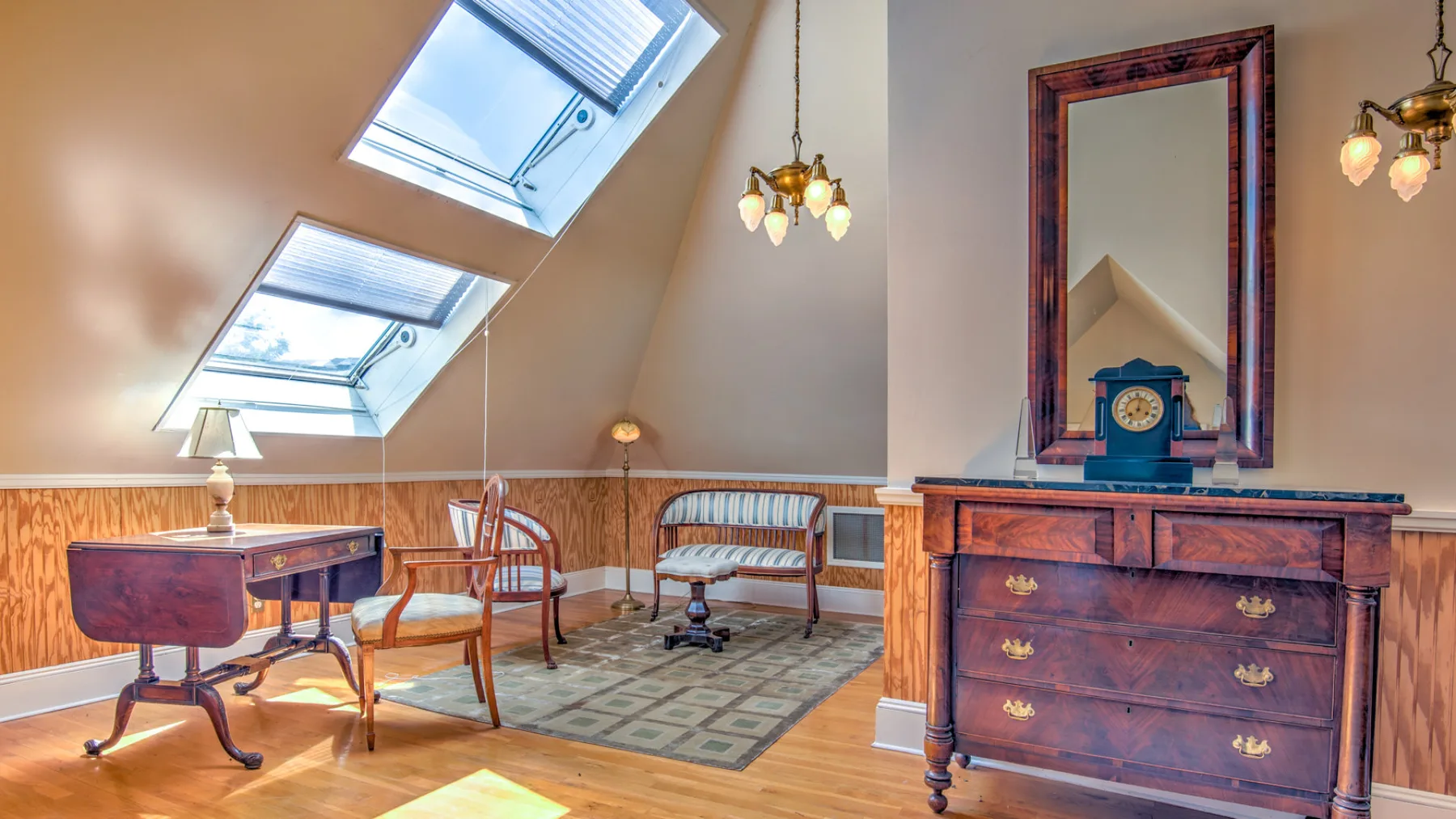 A furnished attic room with sloped skylights, seating, and a wooden dresser.