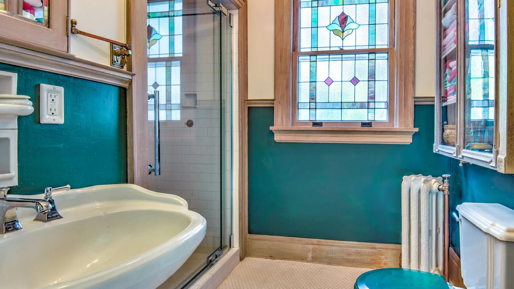 A bathroom with a double sink, teal walls, and stained-glass windows.