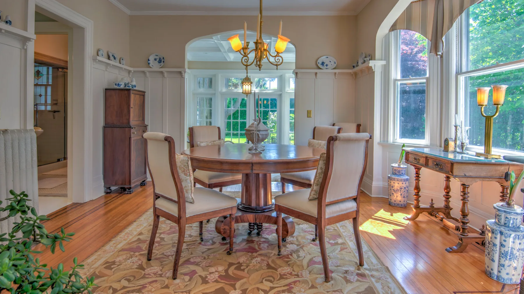 A dining room with a wooden table and upholstered seating beneath a chandelier.