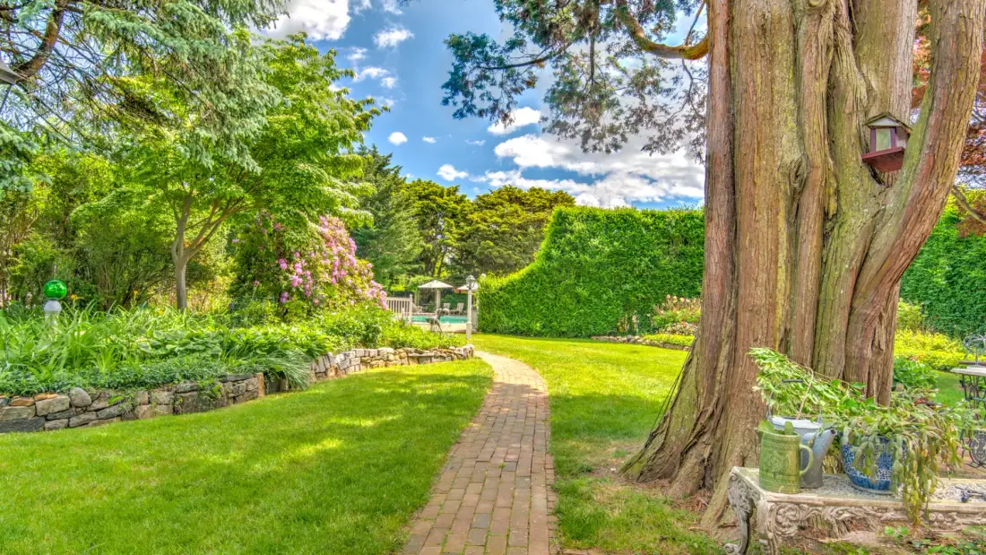 A garden path curves through green lawn and leafy trees.