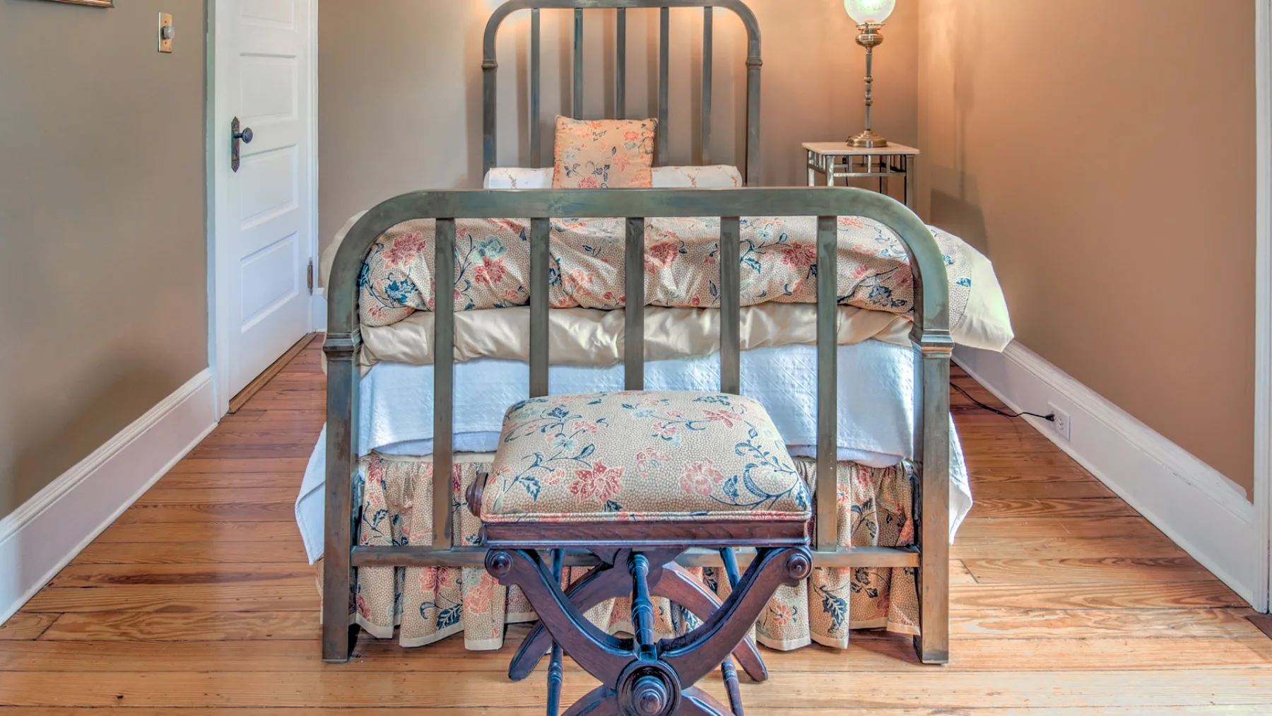 A bedroom with a metal bed, floral bedding, and a small bedside lamp.