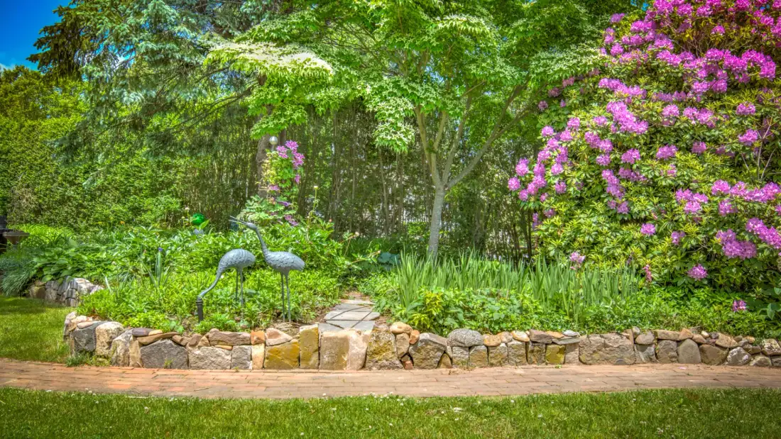 A landscaped garden with flowering shrubs, trees, and two lawn ornaments.