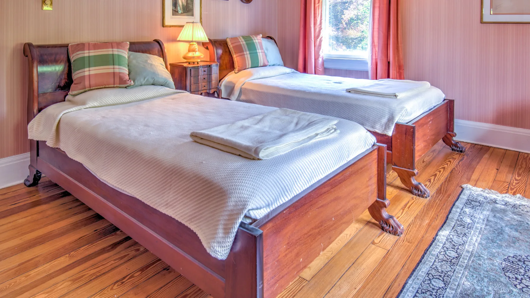 A bedroom with two beds, striped pillows, and a window with curtains.