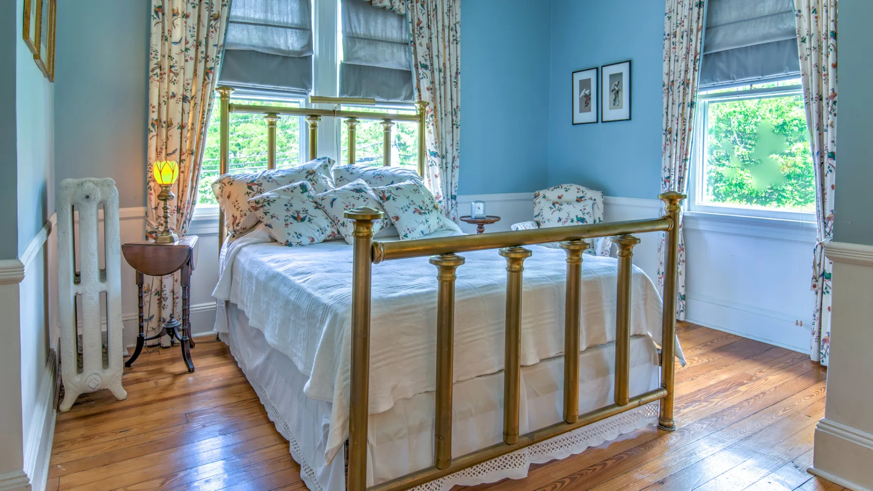 A bedroom with a brass bed, floral bedding, and tall windows.