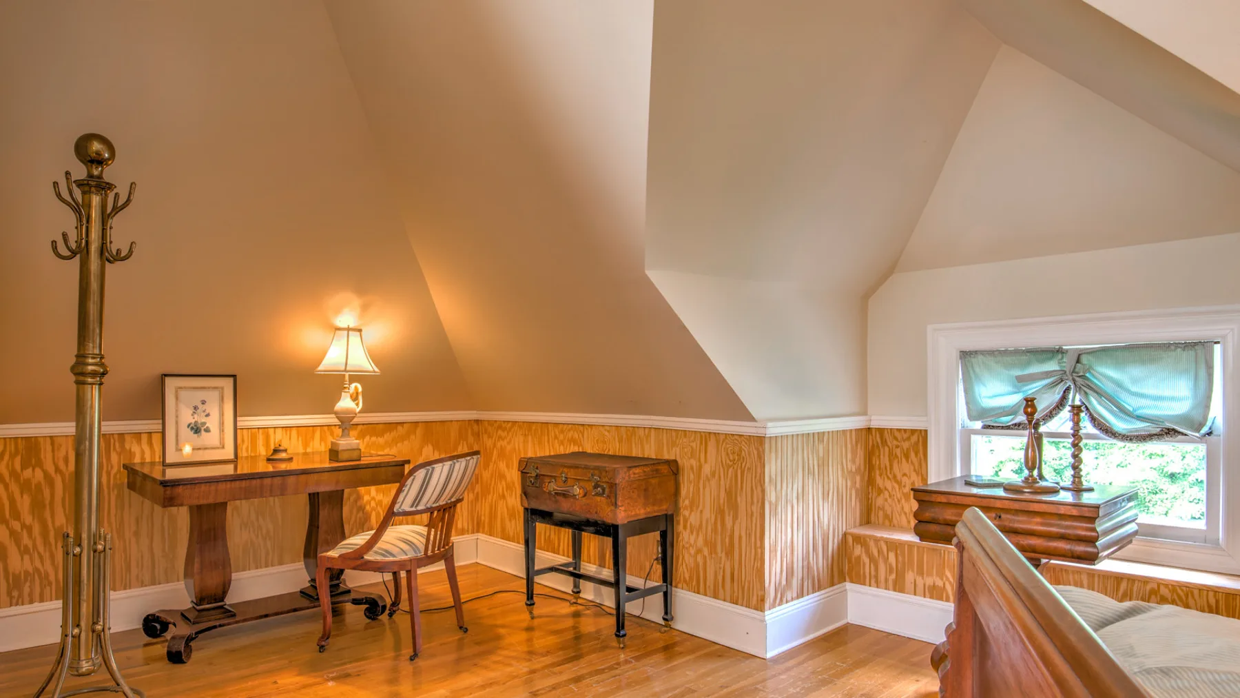 A small attic room has a desk, chair, coat rack, and window.