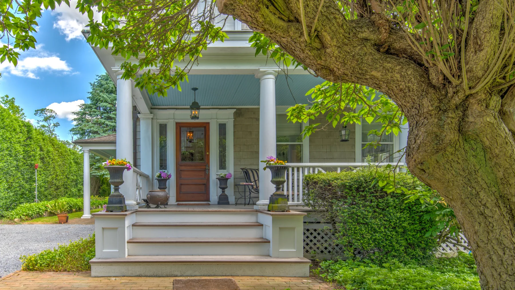 A leafy front porch with white columns, steps, and a wooden door.
