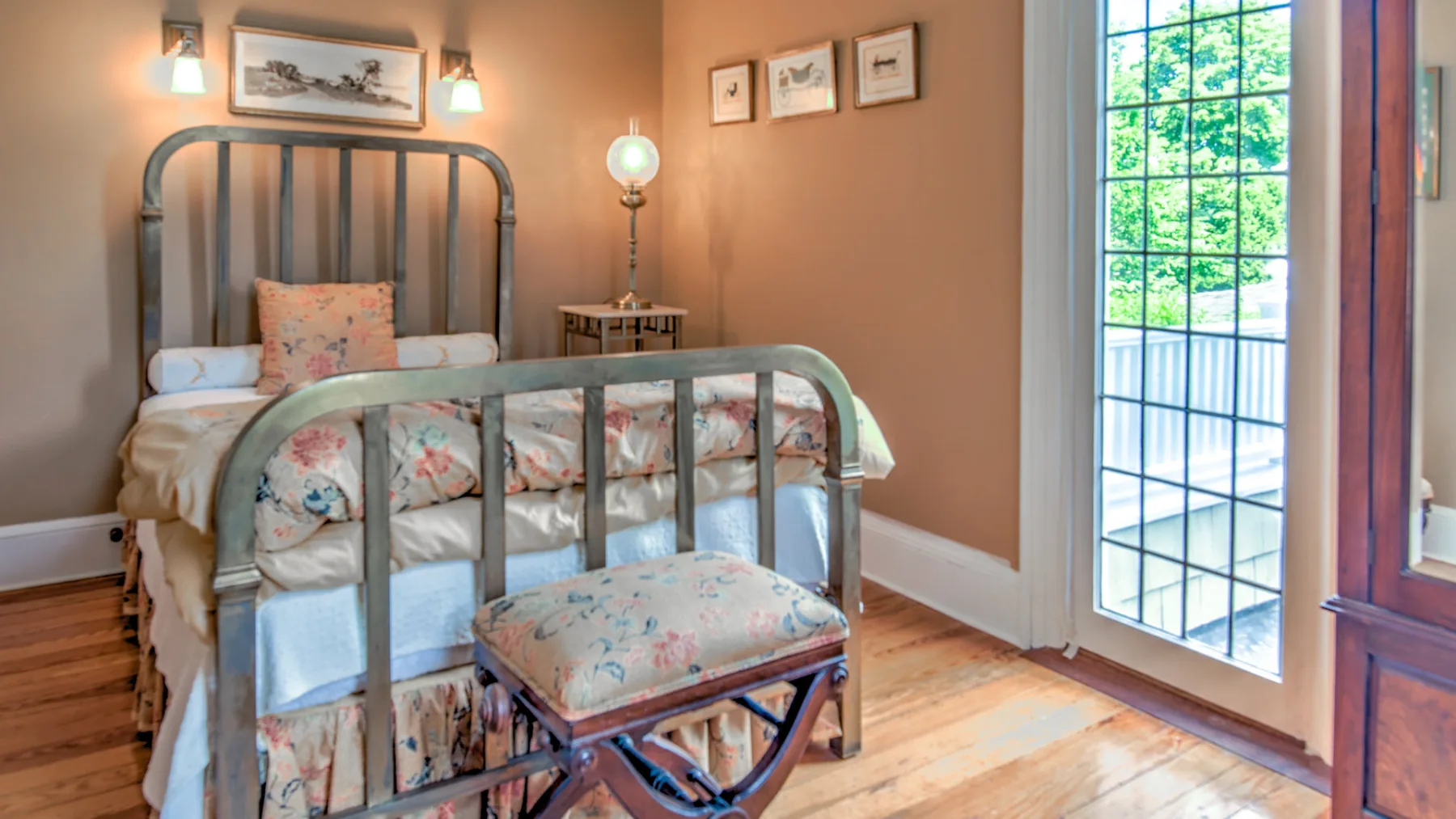 A bedroom with metal beds, floral bedding, and a bright glass door.