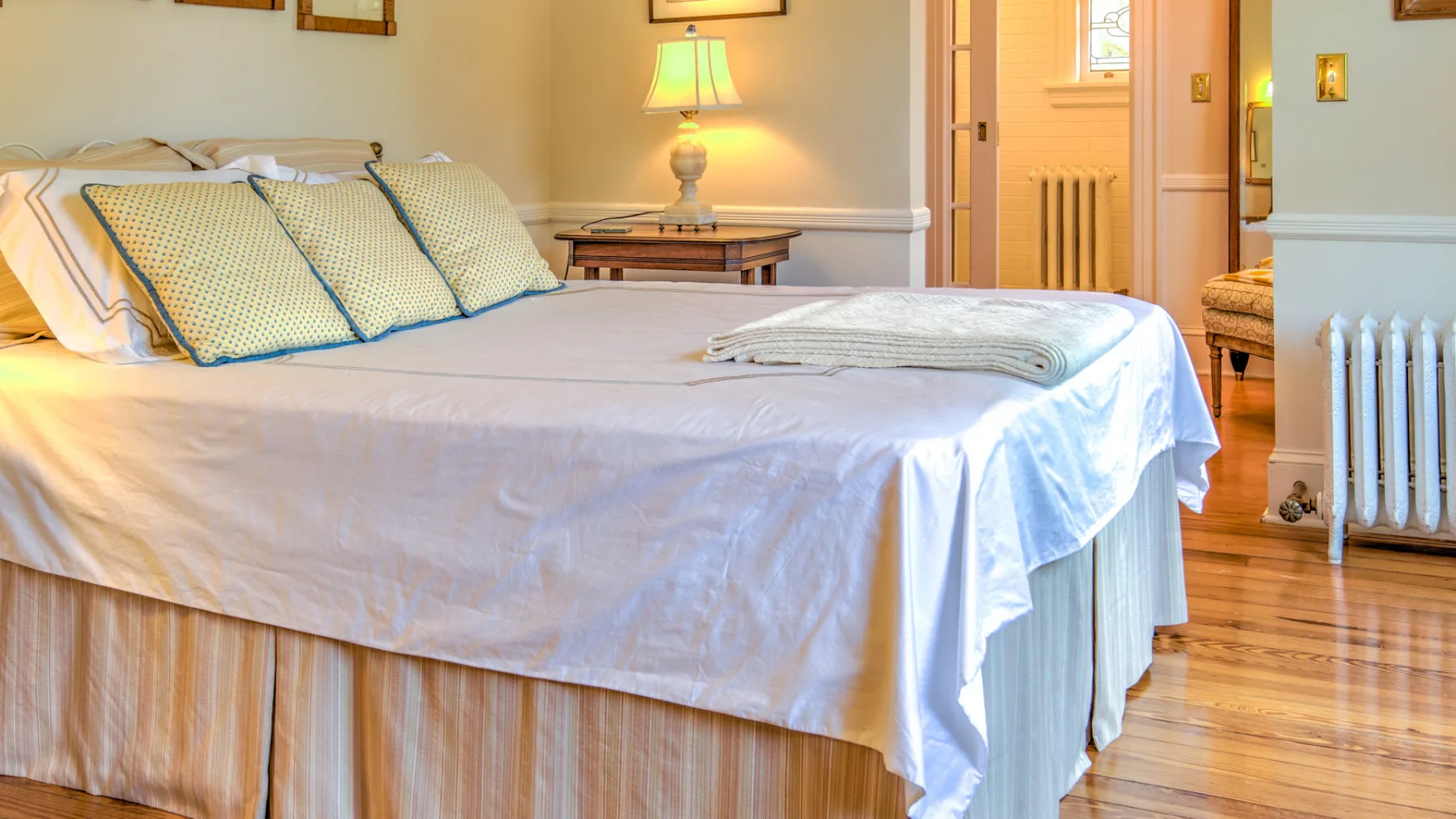 A bedroom with a neatly made bed and a lit bedside lamp.