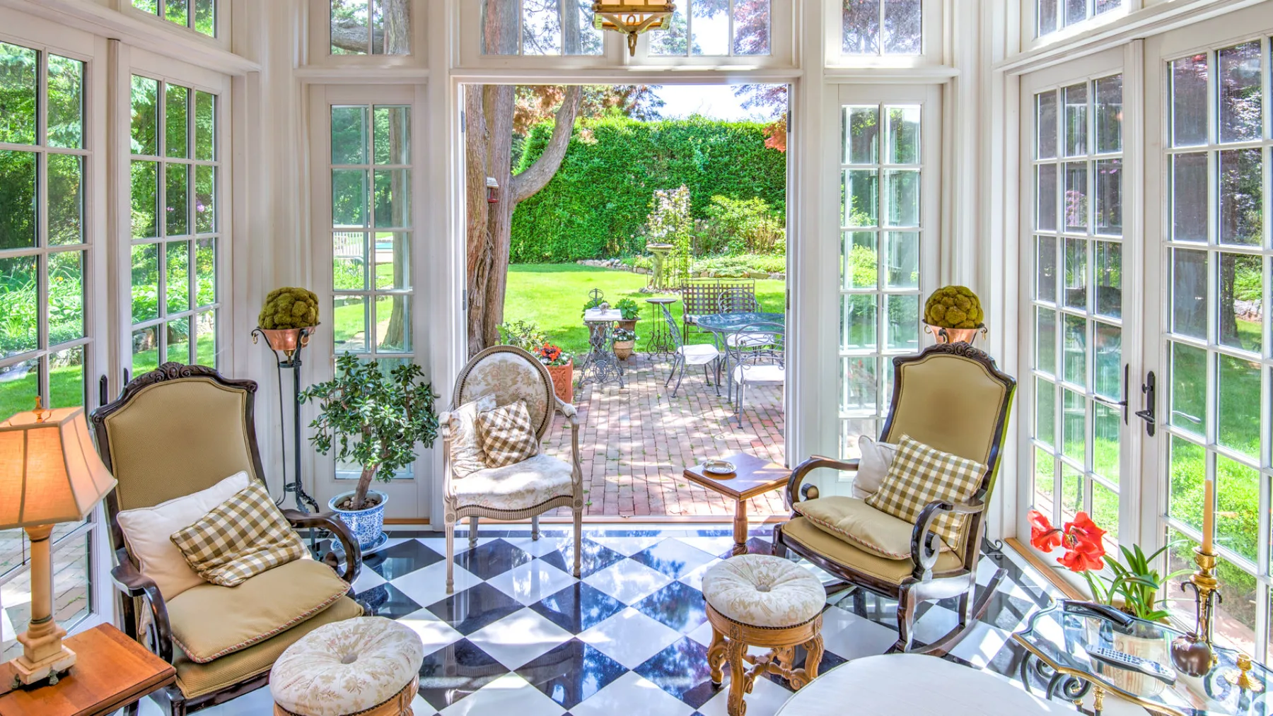 A bright sunroom with seating and large windows overlooking a garden patio.