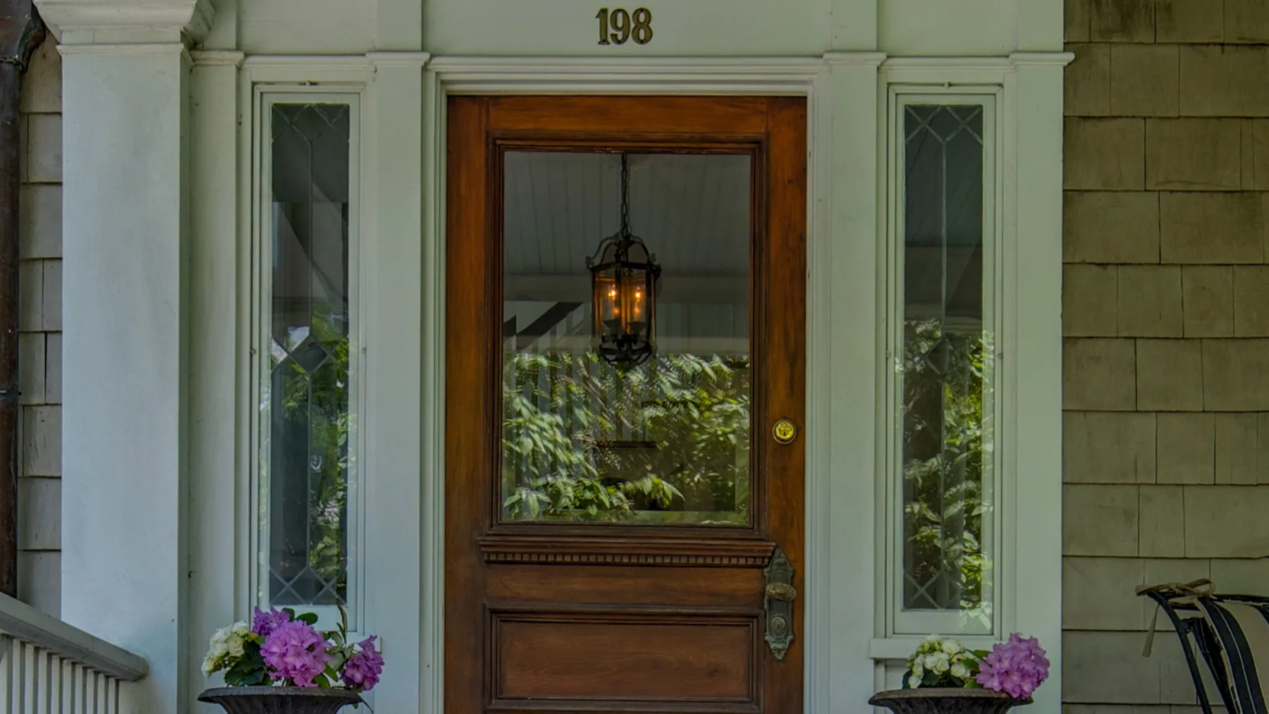 A wooden entrance door with glass panels is framed by pale stone and flowers.