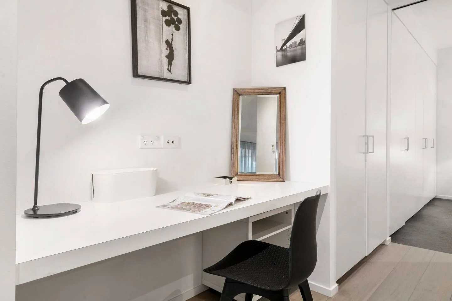 A desk with a chair and lamp sits beside a row of white cabinets.