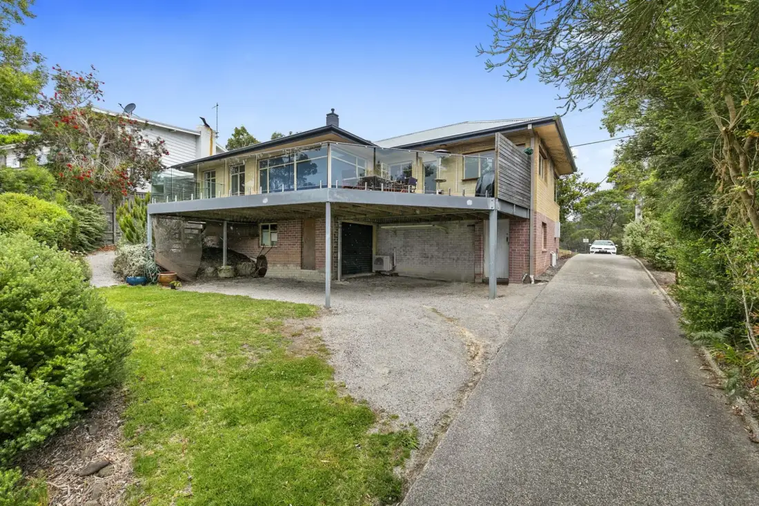 Una casa moderna con una terraza elevada con frente de vidrio junto a una entrada para vehículos.
