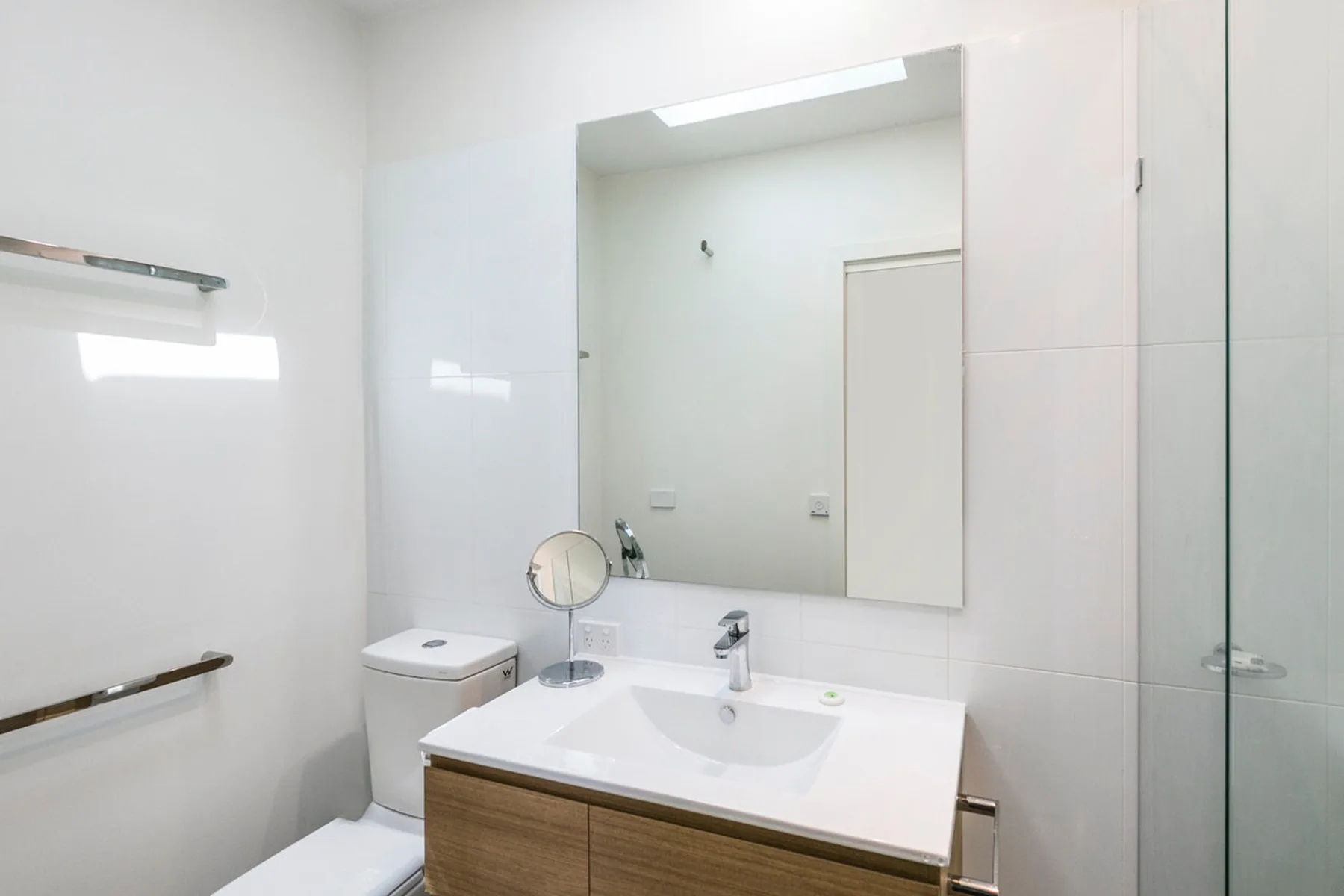 Un baño luminoso con lavabo, espejo y ducha de vidrio.