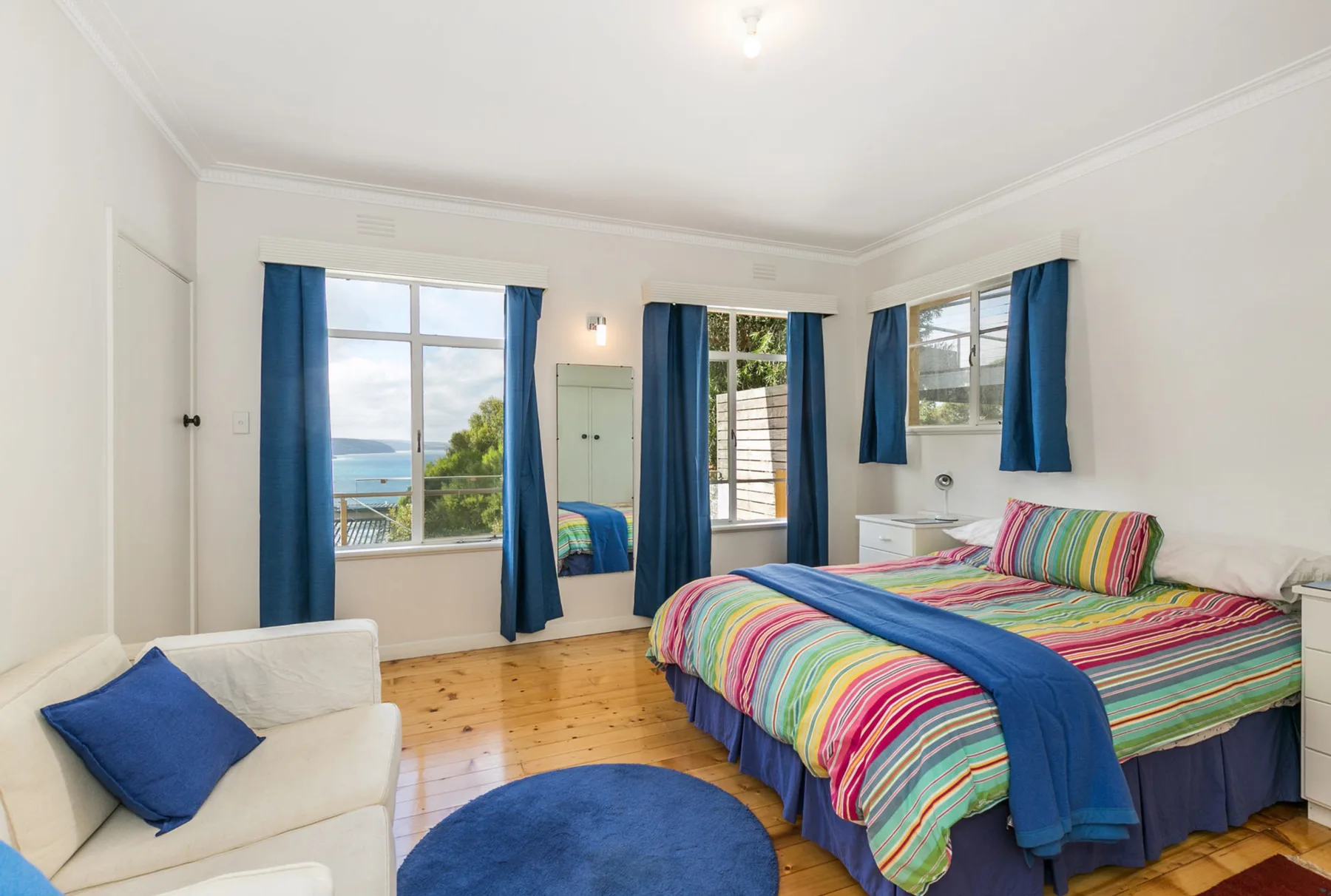 Un dormitorio luminoso con ropa de cama a rayas de colores y cortinas azules.