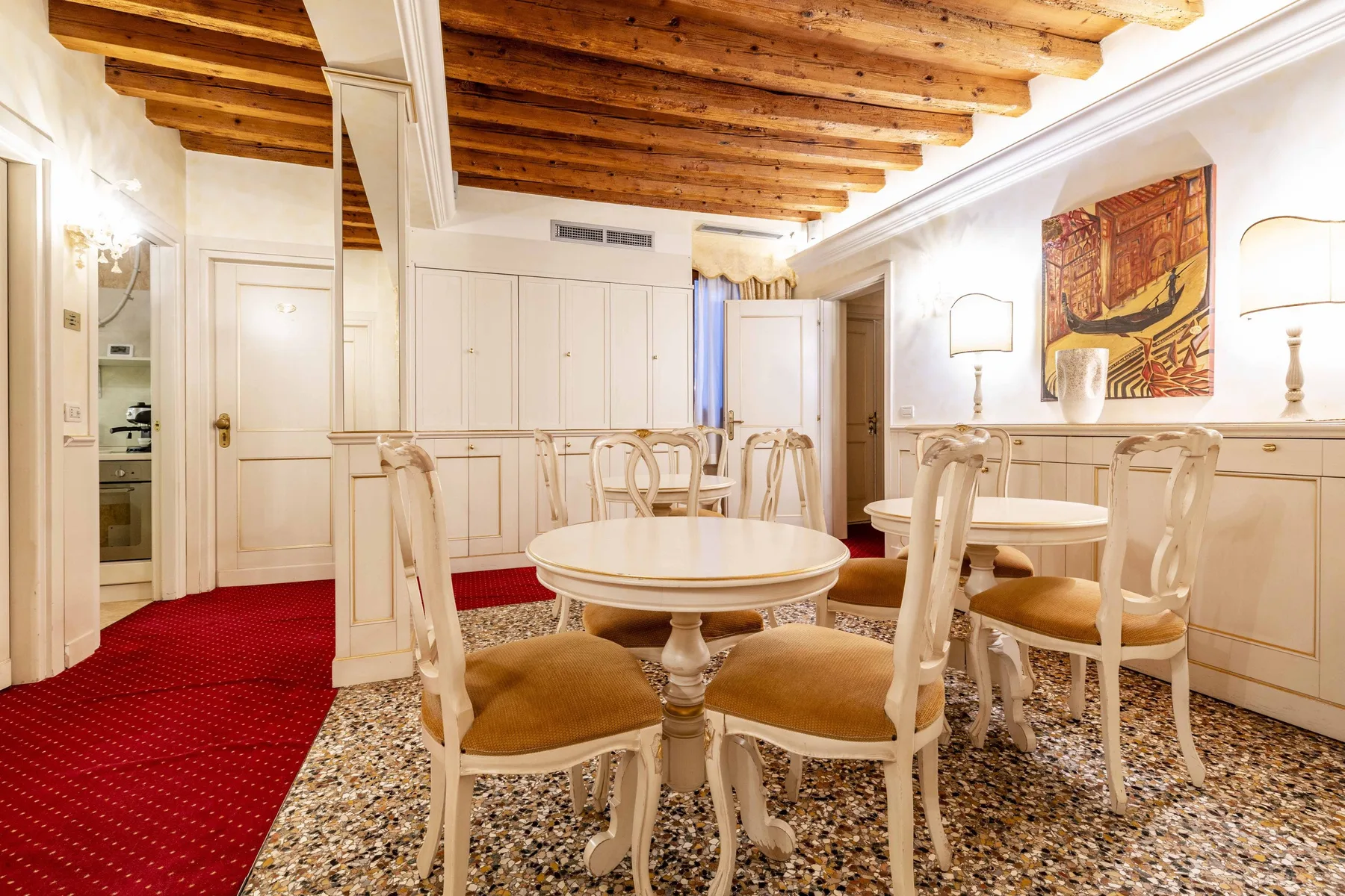 A dining room with a round table, chairs, and exposed wooden ceiling beams.