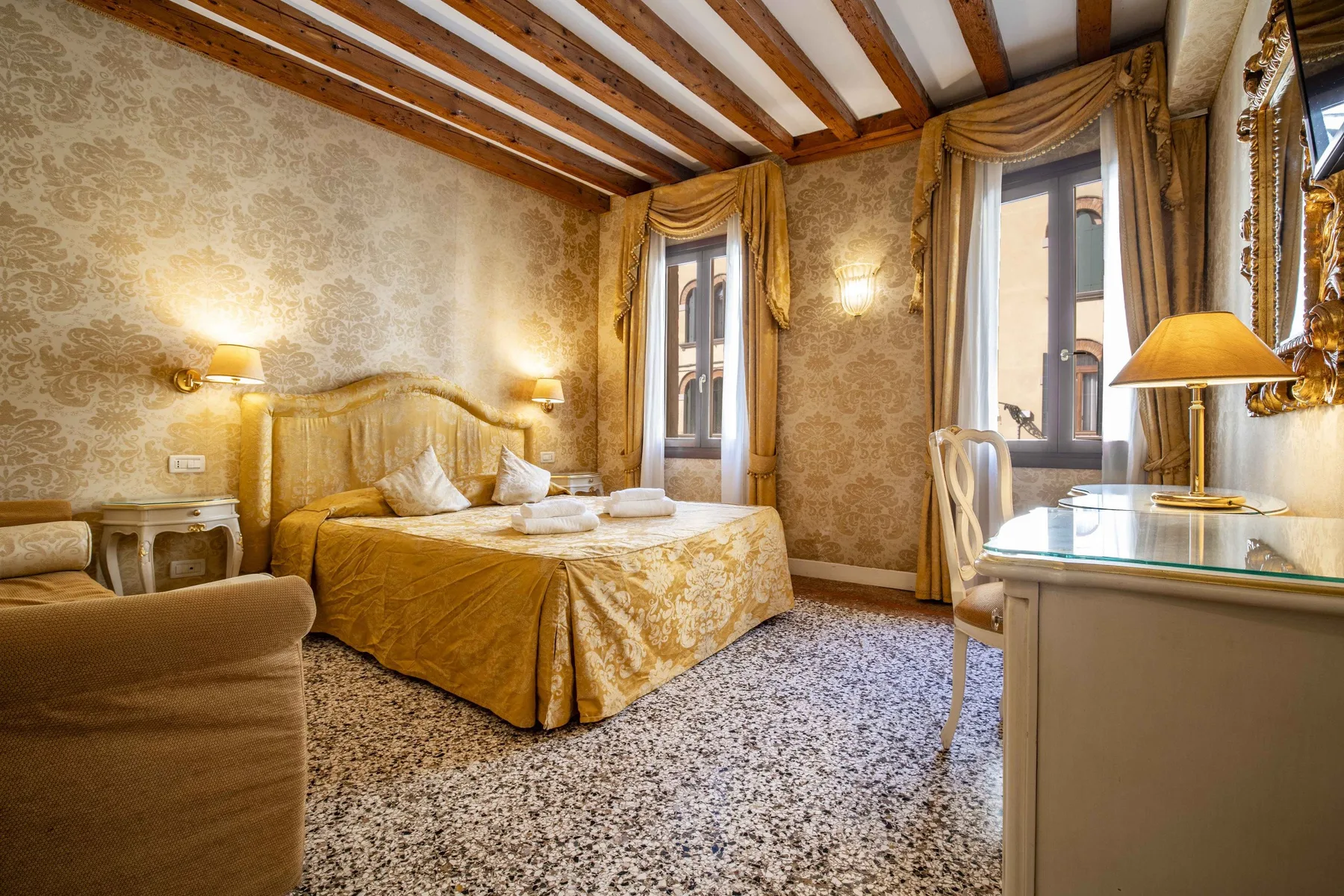 A furnished bedroom with a bed, patterned walls, and tall curtained windows.