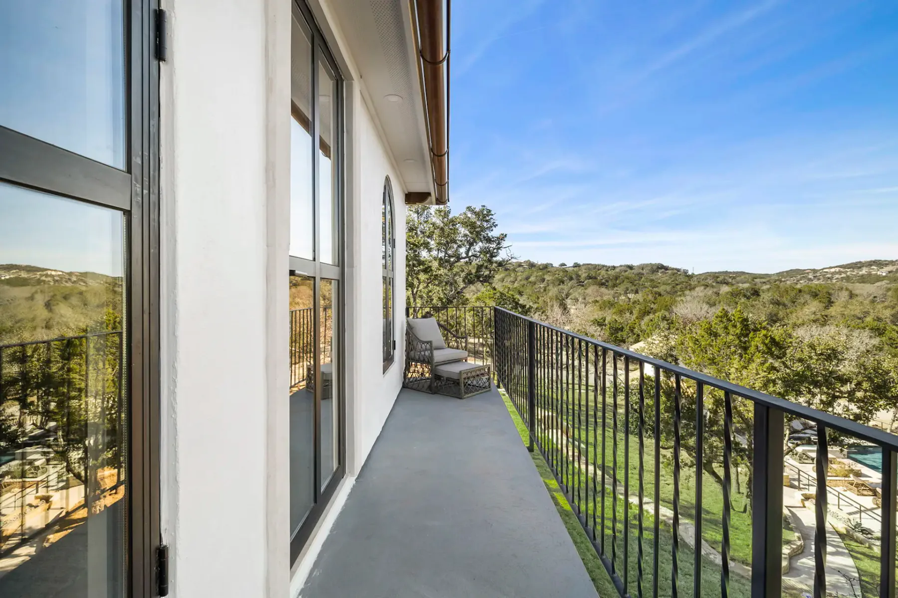 A narrow balcony with outdoor seating overlooks a green, tree-covered landscape.