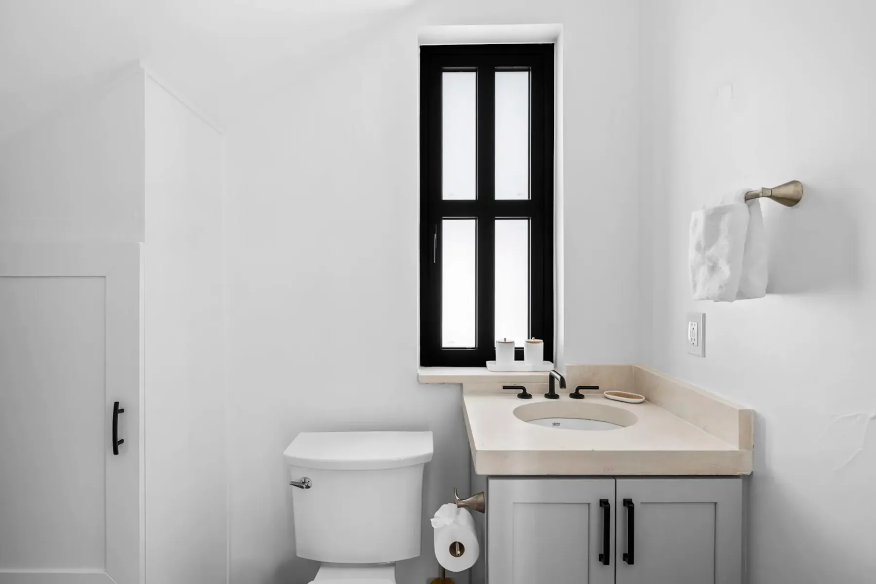 Minimalist bathroom with white walls, a small window, toilet, light gray vanity with a beige countertop, and a towel hanging on the wall.