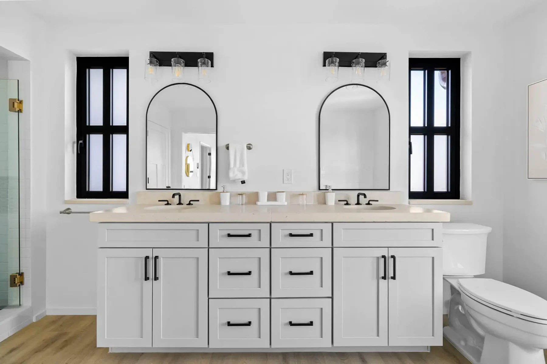 A bright bathroom with a long white vanity, two mirrors, and a toilet.