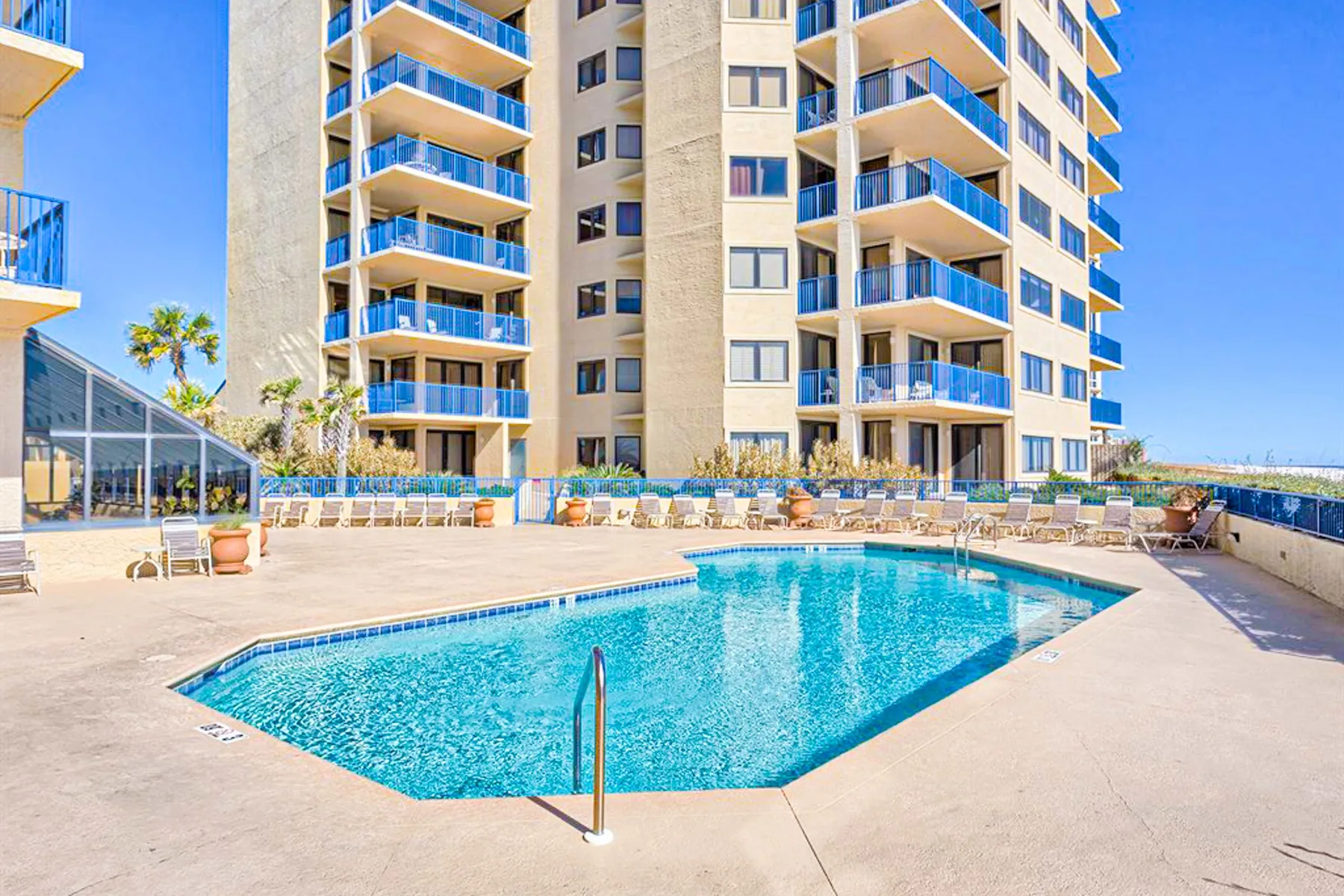 Una piscina y su terraza están junto a un edificio alto de apartamentos.