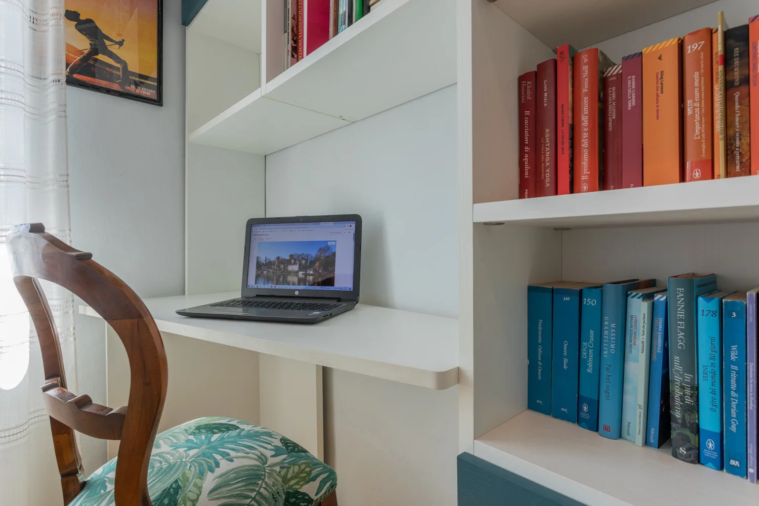 Un escritorio empotrado con una computadora portátil abierta está junto a estantes con libros.