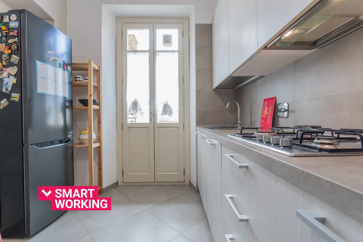 Una cocina estrecha con gabinetes blancos, un refrigerador y una estufa de gas.