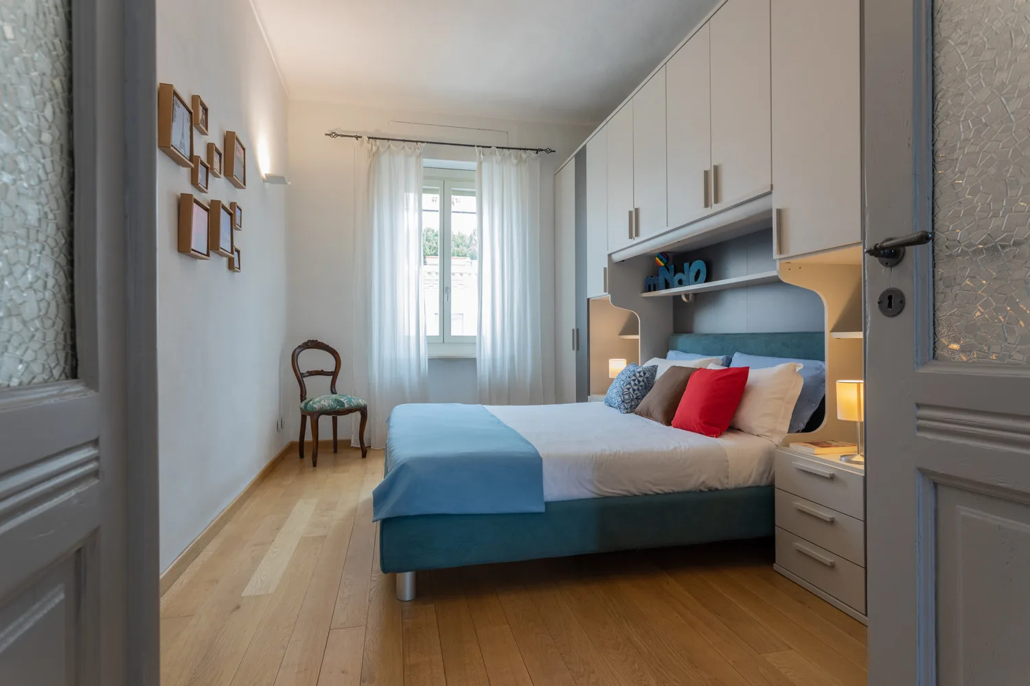 Un dormitorio con una cama, armarios empotrados y una ventana con cortinas transparentes.