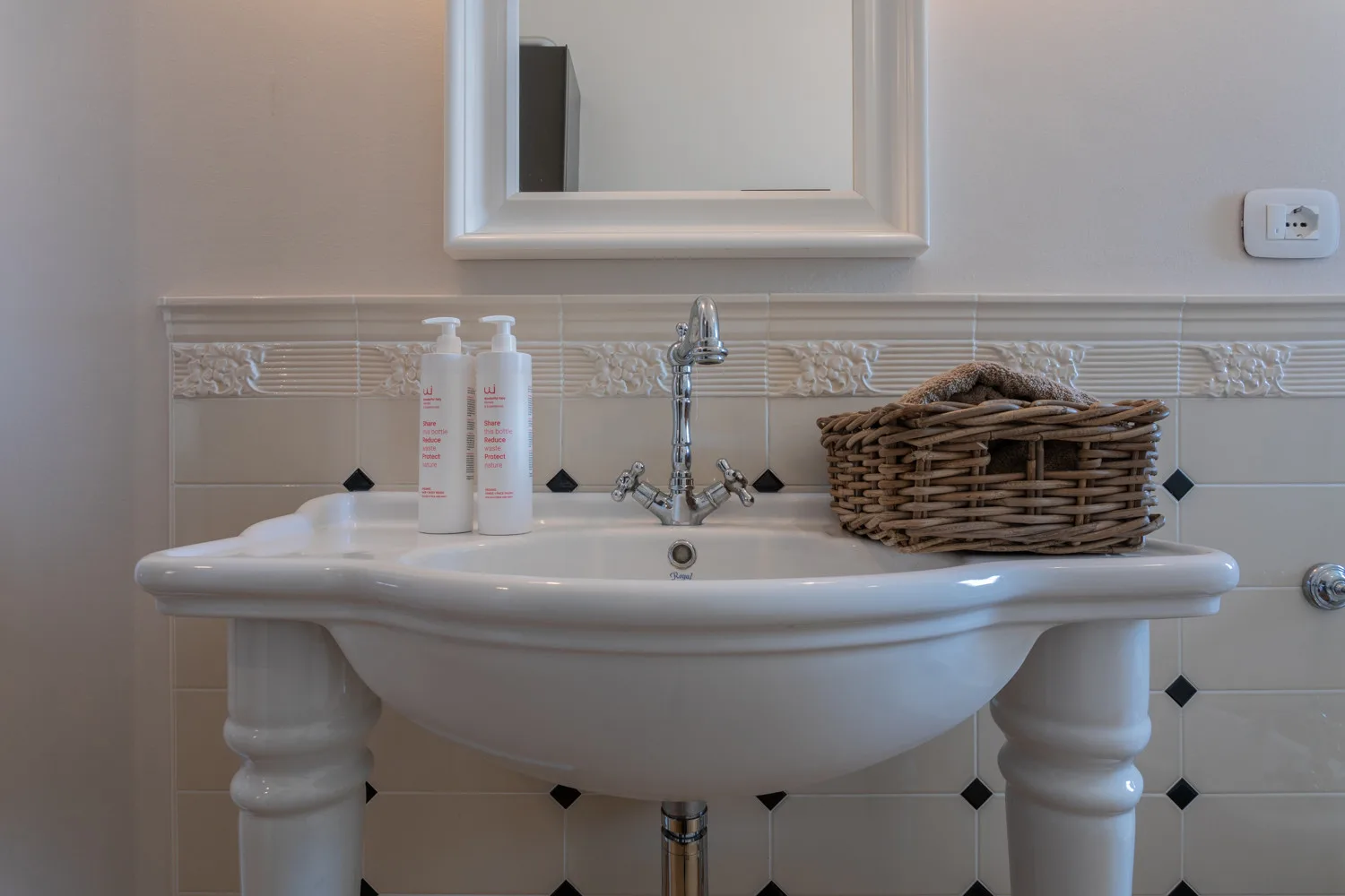 Un lavabo de baño con un espejo en la pared y una cesta de mimbre sobre la pila.