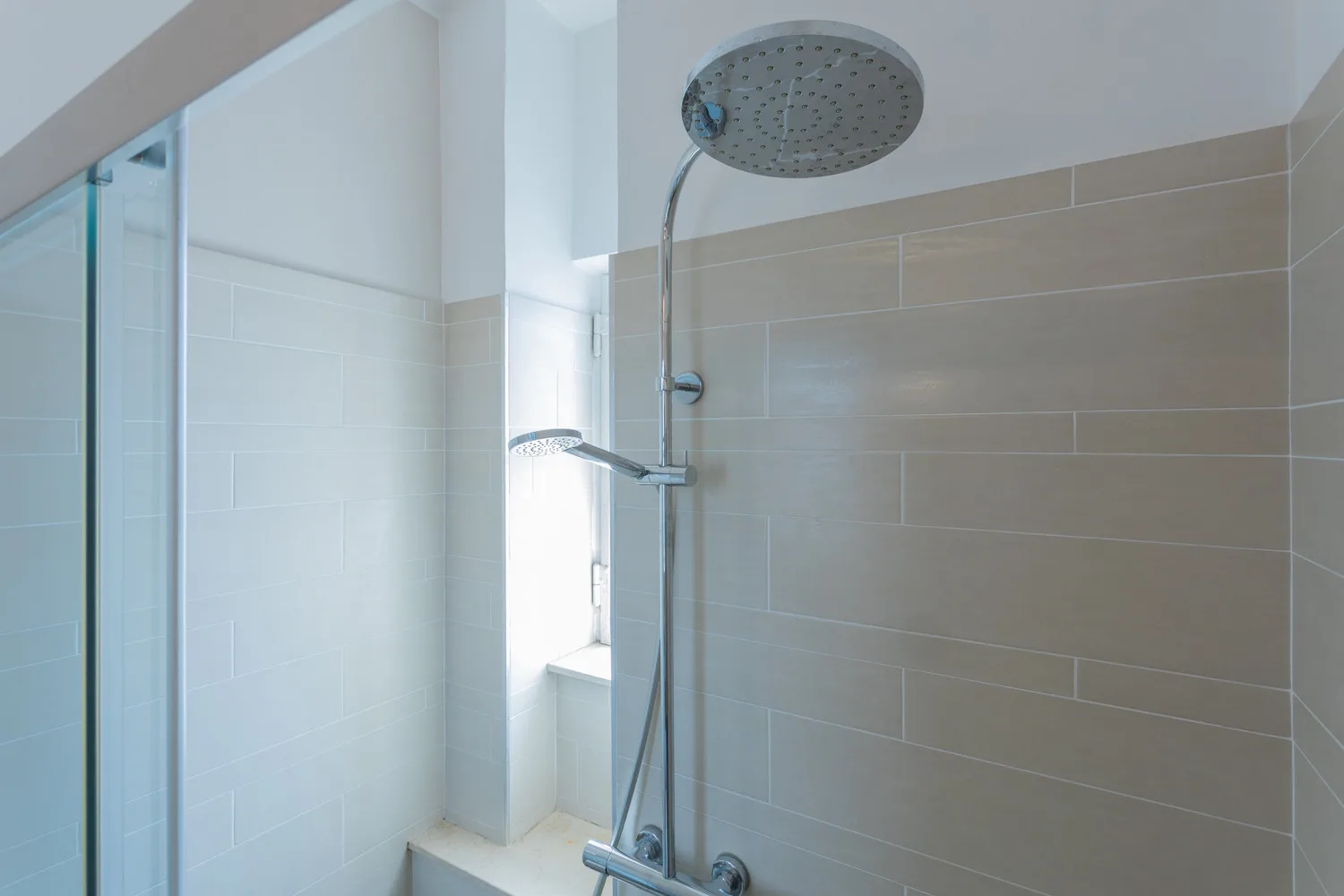 Una ducha de baño con azulejos y un amplio cabezal de ducha redondo.