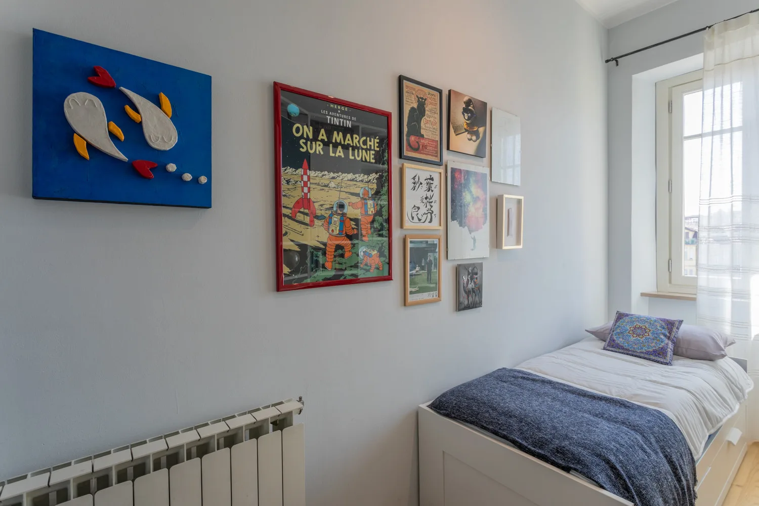 Un dormitorio con una cama bajo cuadros enmarcados, junto a una ventana luminosa.