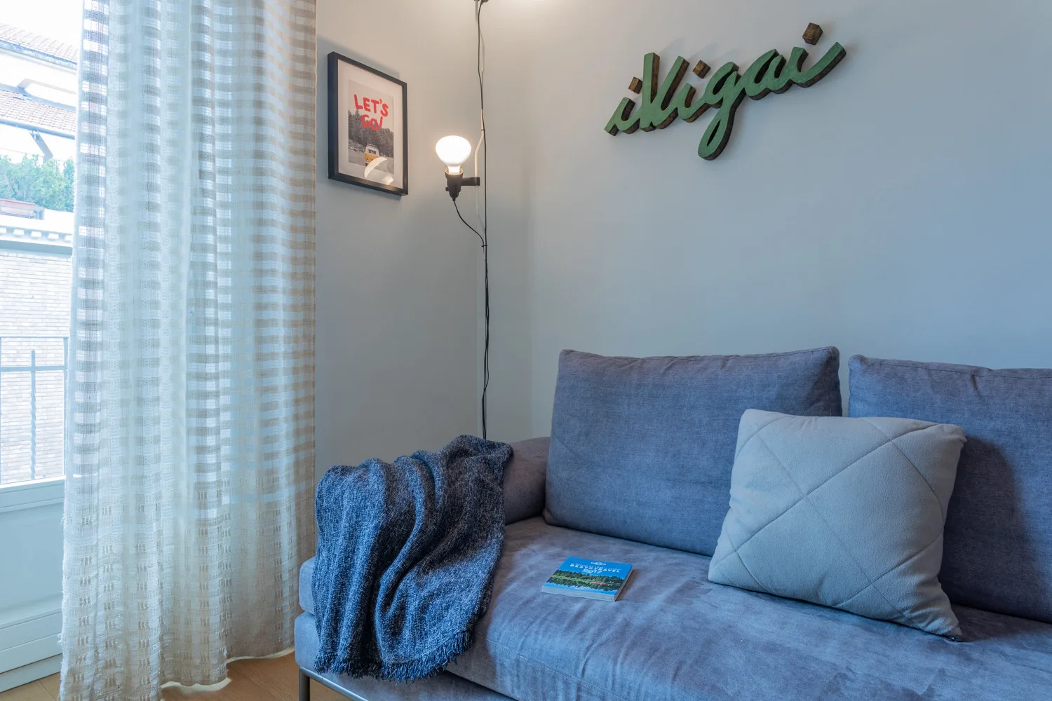 Una zona de estar con un sofá azul junto a una ventana luminosa.