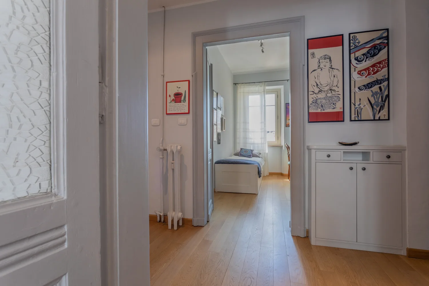 Un pasillo da a una habitación luminosa con una cama y un armario blanco.