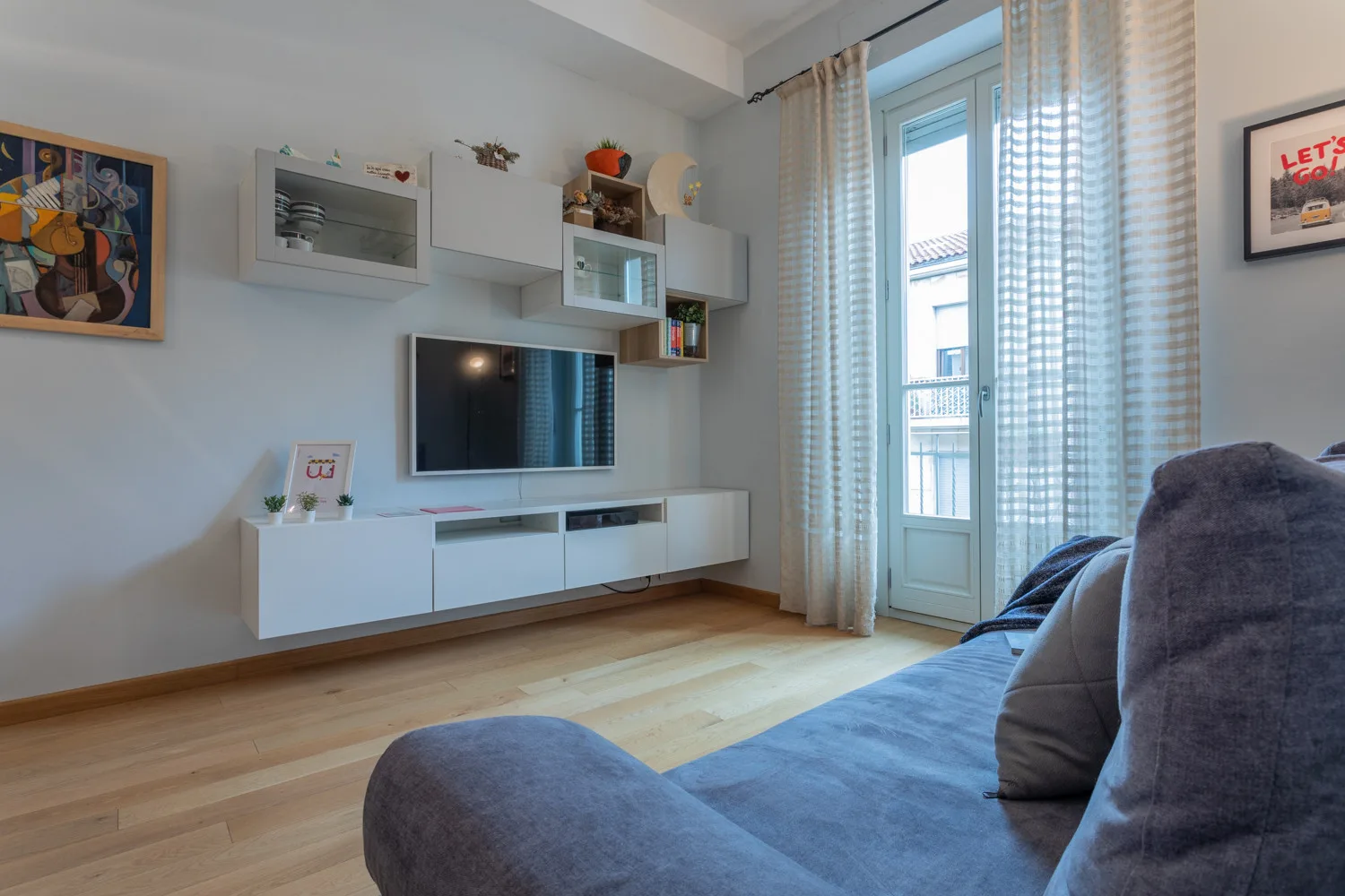Una sala de estar con televisor, asientos y ventanas altas.