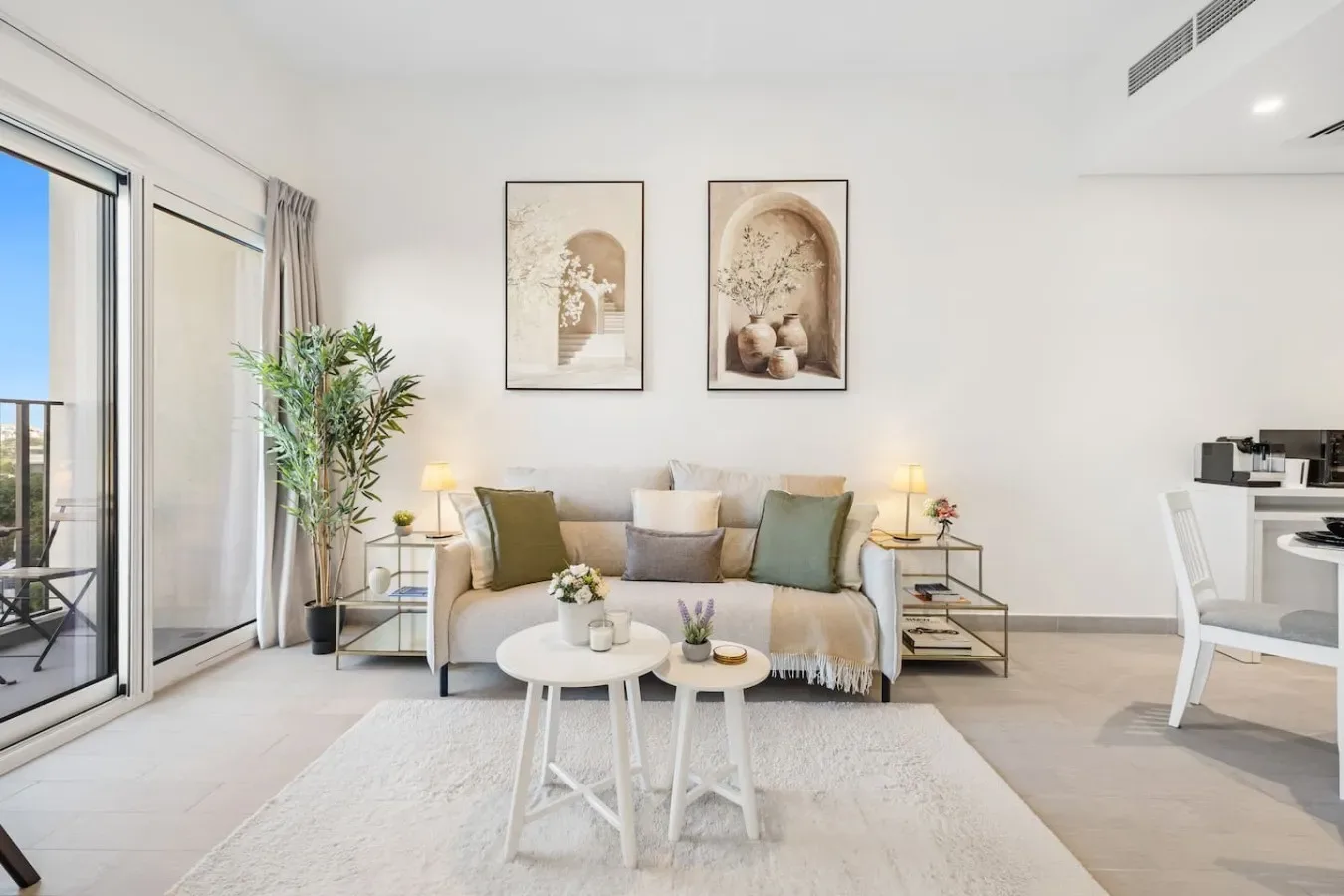 Una sala luminosa con un sofá, dos mesas pequeñas y puertas corredizas de vidrio.