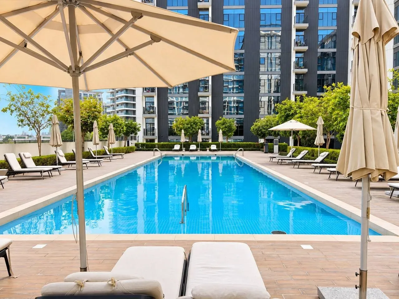 Una piscina al aire libre está rodeada de asientos reclinables y sombrillas.