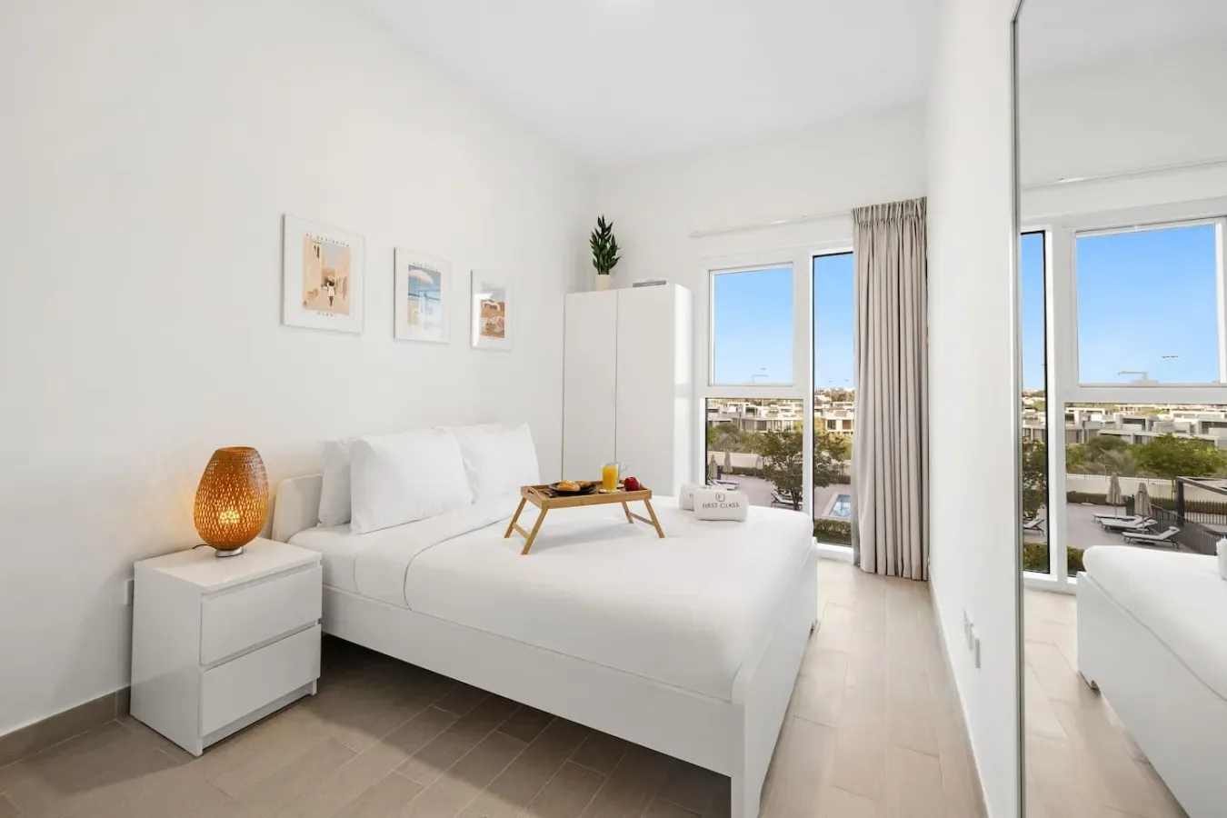 Un dormitorio luminoso con una cama blanca, una mesita de noche y puertas de vidrio hacia un balcón.