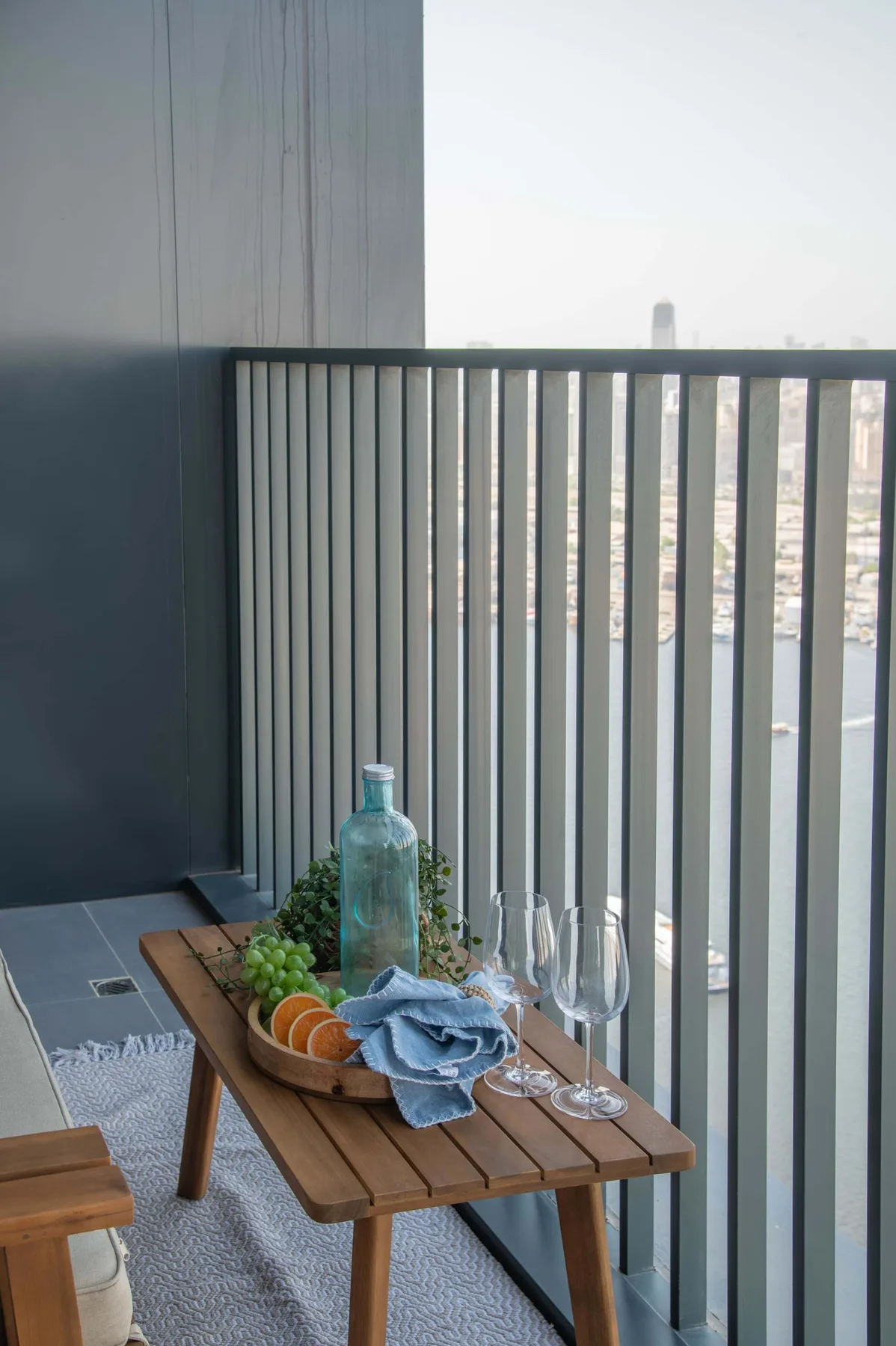 Una pequeña zona de estar en un balcón, con una mesa de madera y bebidas junto a la barandilla.