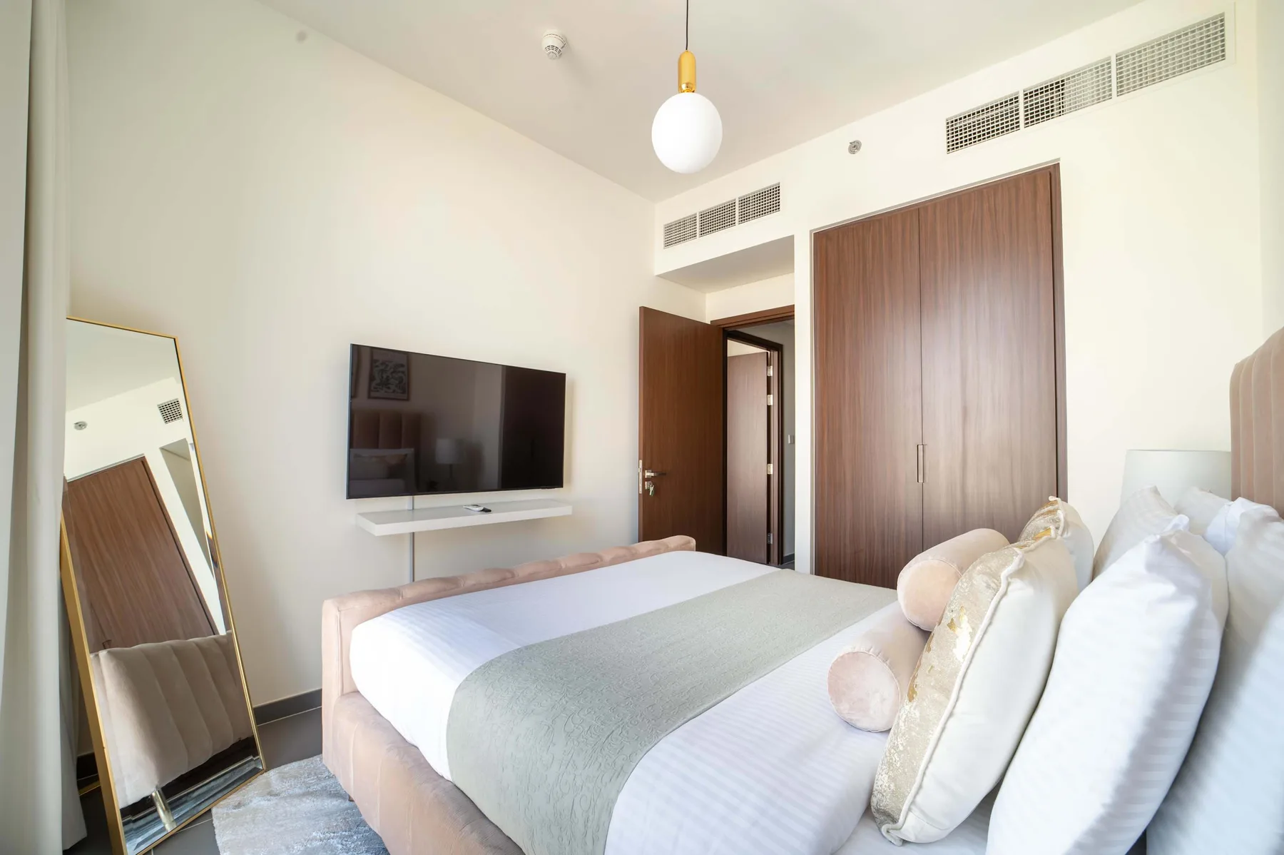 Un dormitorio con una cama tendida, un televisor en la pared y un espejo de cuerpo entero.
