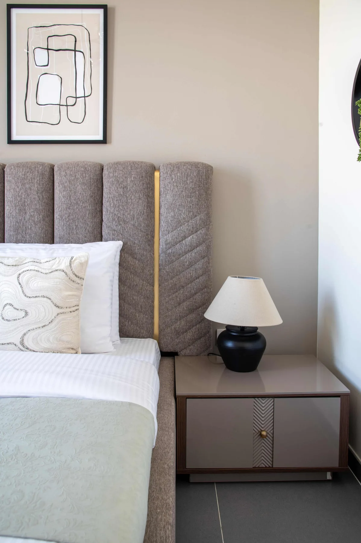 Un dormitorio con cama, cabecero tapizado y mesita de noche.