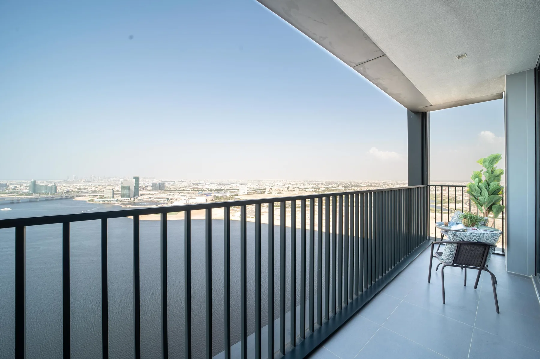 Un balcón con barandillas oscuras da a una extensión de agua y un horizonte urbano lejano.