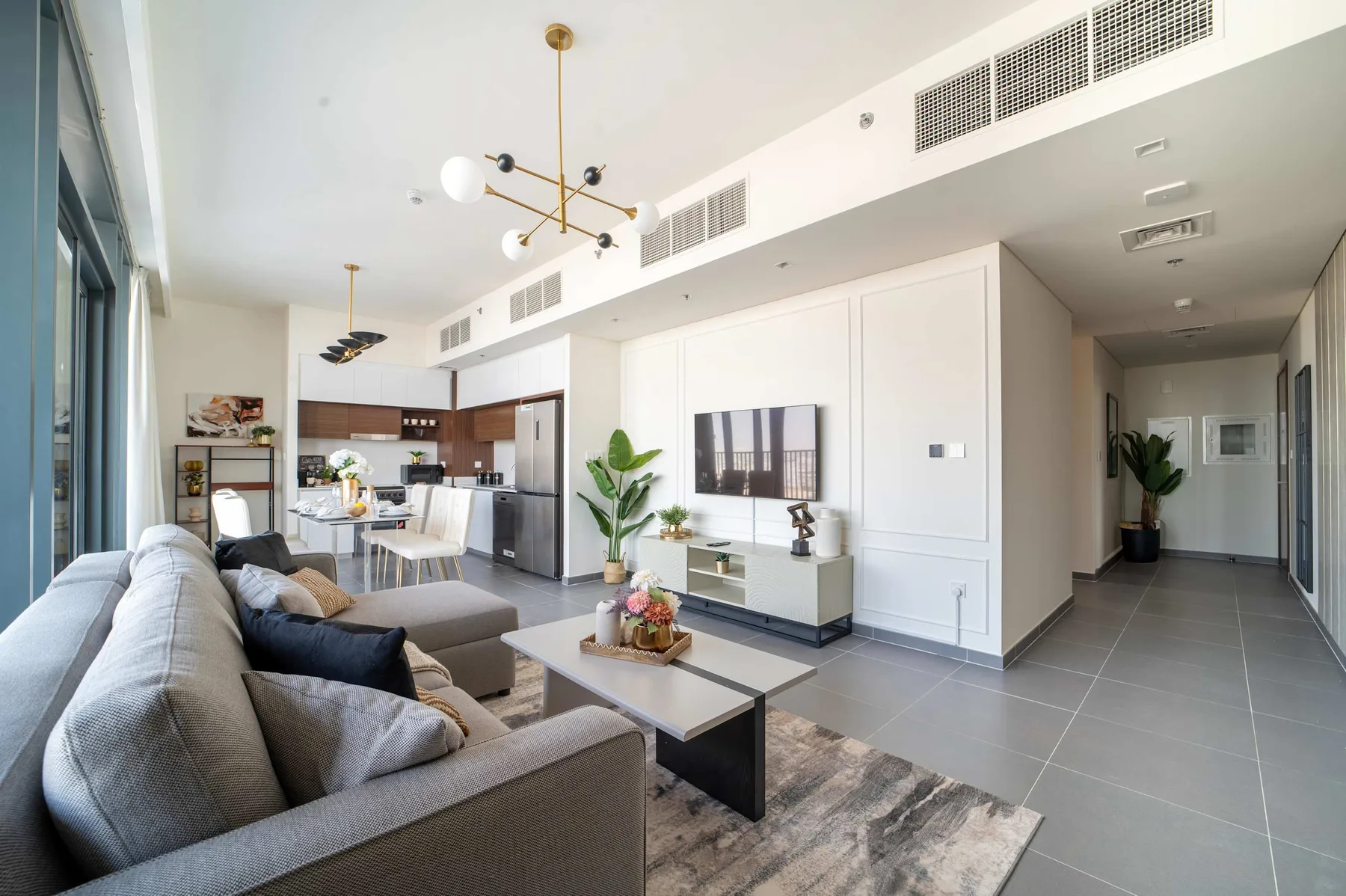 A bright living room with seating, a television, and an open kitchen.