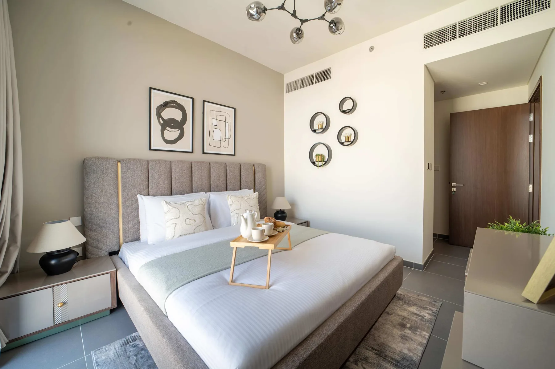 Un dormitorio con una cama tendida, cuadros en la pared y una puerta.