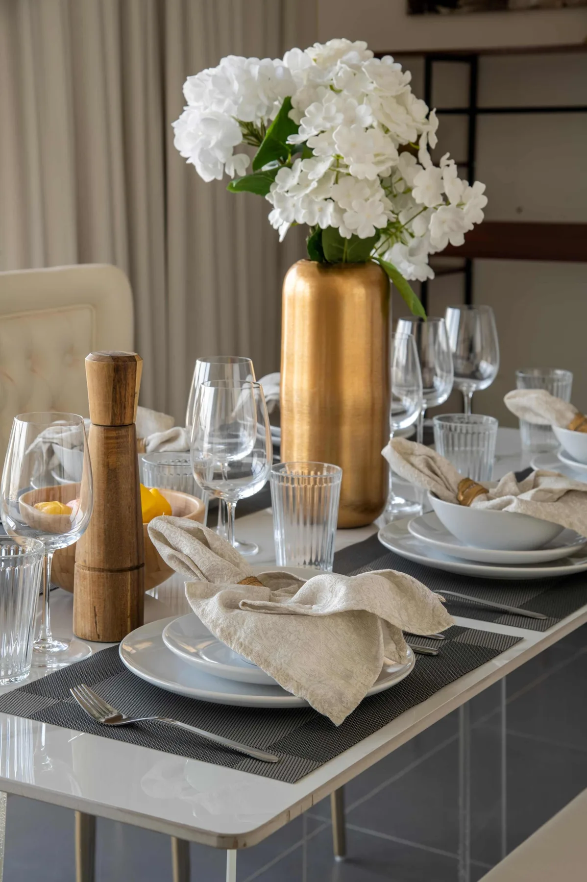 Una mesa de comedor está puesta con platos, vasos, servilletas dobladas y flores blancas.