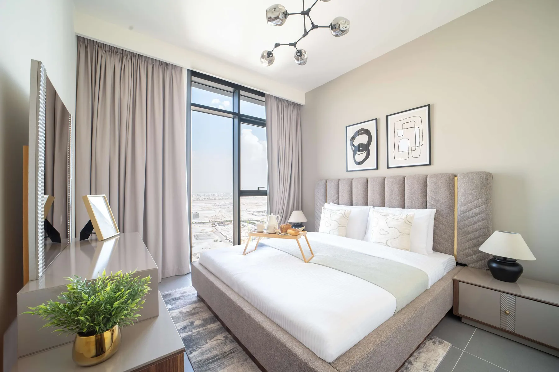 Dormitorio luminoso con una cama grande, una ventana alta y cortinas largas.